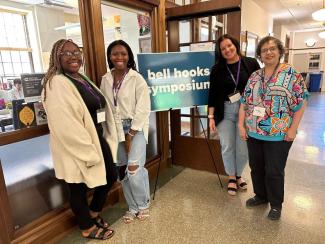 Panelists stand next to bell hooks center sign