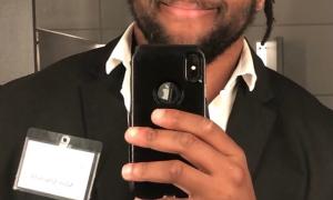 Adam Jenkins with black suit white shirt and locs in a bun